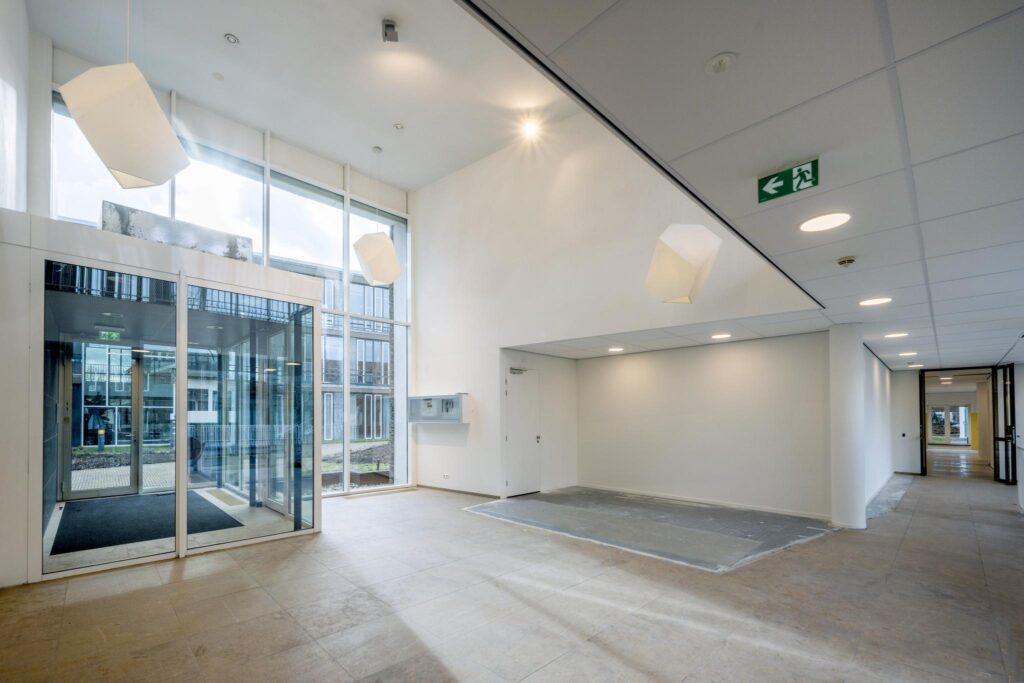 Moderne, lichte entreehal van een kantoorgebouw aan de De Cuserstraat met glazen deuren en hoge ramen.